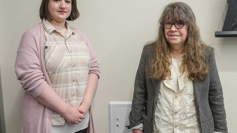 Two women stand in front of a wall in a conference room.