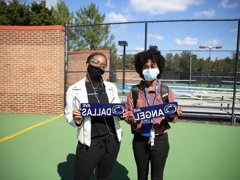 Two female students wearing masks and holding signs with their names.