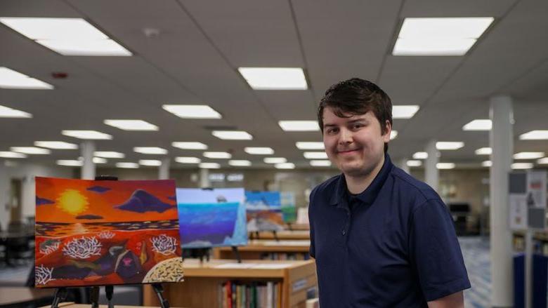 Jacob Campbell st和ing next to his painting