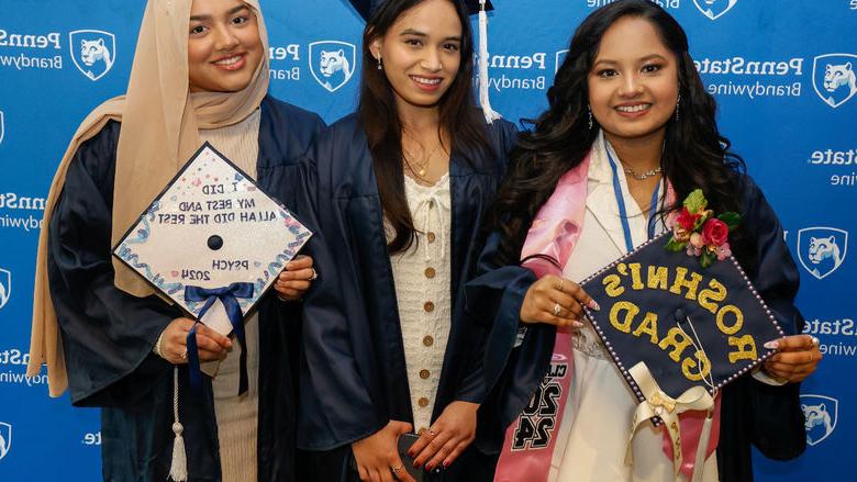 Three female students pose for a photo wearing their commencement gowns.