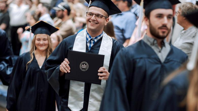 New Penn State graduate Kolton Lyons, who earned an associate degree in business administration, proudly displays his degree to onlooking family and friends during the commencement ceremony at Penn State DuBois.