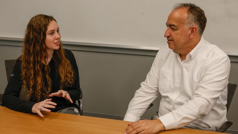 Two people sit at a table in a conference room.